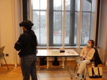 Tess  Eschebach sits watching a participant viewing her project, "Consume," with a Virtual Reality headset.